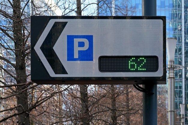 Panneau de signalisation indiquant le nombre de places de stationnement et la flèche pointant vers le parking, le texte peut être ajouté à l'espace blanc, aux arbres flous et à l'arrière-plan des bâtiments.