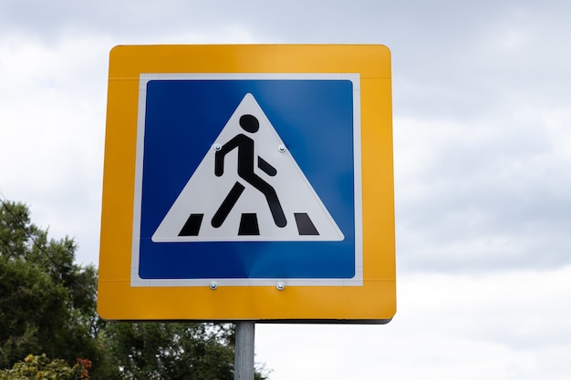 Photo panneau de signalisation de passage pour piétons dans un cadre jaune sur ciel gris