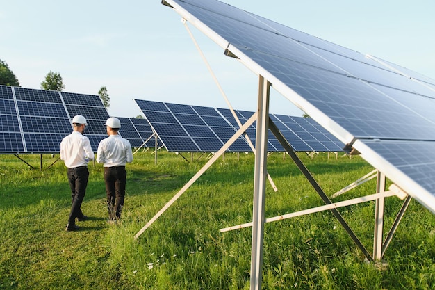 Le panneau solaire de la ferme solaire avec deux ingénieurs à pied pour vérifier le fonctionnement du système Énergie alternative pour conserver l'énergie mondiale Idée de module photovoltaïque pour la production d'énergie propre