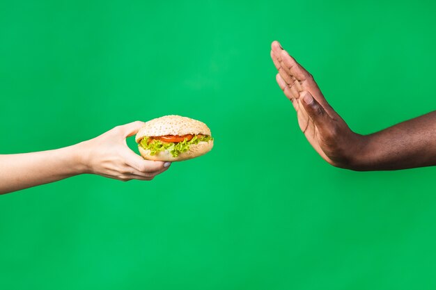 Panneau stop. Image recadrée en gros plan d'un homme noir afro-américain rejetant un hamburger malsain isolé sur fond vert.