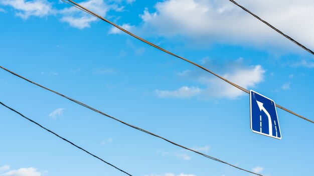 Panneau de virage à gauche accroché sur fil sur fond de ciel bleu