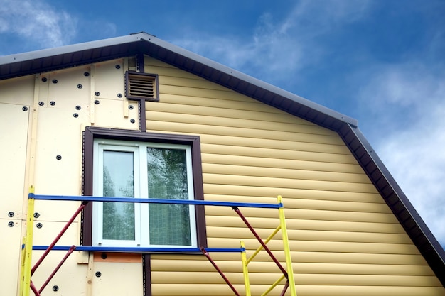 Panneaux de parement beige montage avec échafaudage sur le dessus de la maison rurale