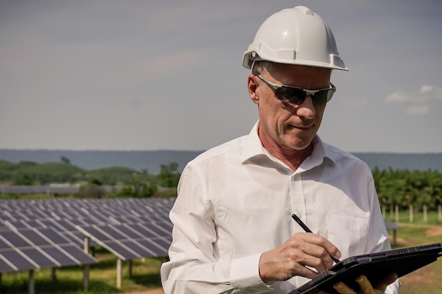 Panneaux solaires de ferme solaire avec des ingénieurs utilisant une tablette pour vérifier le fonctionnement du système Énergie alternative pour la conservation mondiale de l'énergie Concept de module photovoltaïque pour la production d'énergie propre