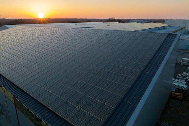 Panneaux solaires photovoltaïques bleus montés sur le toit d'un bâtiment pour produire de l'électricité écologique propre au coucher du soleil Production de concept d'énergie renouvelable