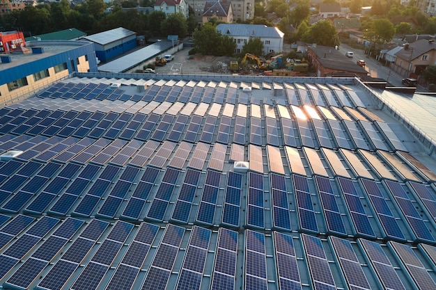 Panneaux solaires photovoltaïques bleus montés sur le toit du bâtiment pour produire de l'électricité écologique propre au coucher du soleil Production de concept d'énergie renouvelable