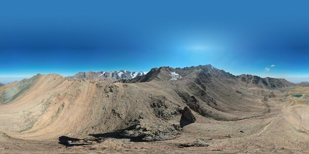 Panorama 360 d'un lac de montagne et de sommets enneigés. Un lac morainique à la couleur d'émeraude.