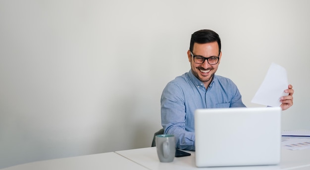 Panorama de la bannière d'un jeune homme d'affaires souriant et joyeux entrepreneur dans un nouveau bureau lumineux travaillant avec un ordinateur portable faisant parler le chat vidéo par conférence téléphonique en ligne