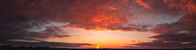 Panorama du coucher de soleil coloré spectaculaire avec des nuages sombres et lumineux. Les rayons du soleil traversent le ciel nuageux. Nuages sombres contre un ciel saturé lumineux.