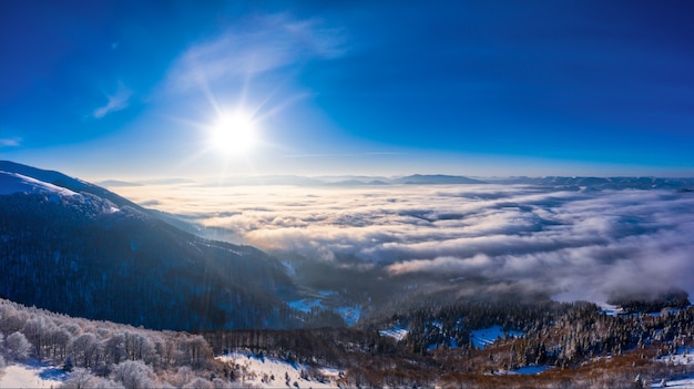 Panorama hivernal pittoresque de collines montagneuses couvertes de neige et de sapins par temps clair et ensoleillé avec le soleil et le ciel bleu. Concept de beauté de la nature vierge. Espace de copie