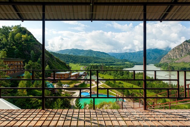 Panorama montagneux : un petit village, un centre de loisirs avec piscine et petites maisons en bois dans les montagnes de l'Altaï, à proximité d'une rivière de montagne et d'une route