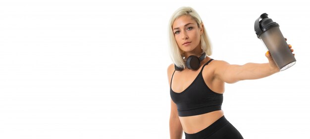 Panorama de sport fille blonde caucasienne avec écouteurs faire du sport et boit de l'eau de la bouteille de sport