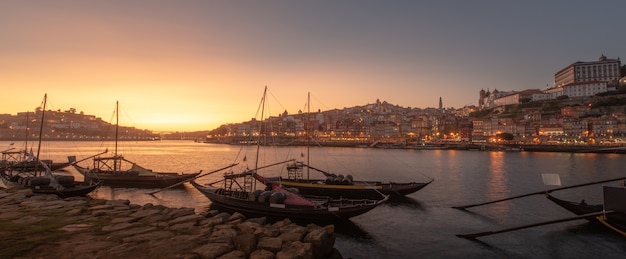 Photo panoramique du paysage urbain de porto au coucher du soleil avec la rivière à l'avant et le navire transporteur de vin en premier plan et la ville de porto en arrière-plan, portugal