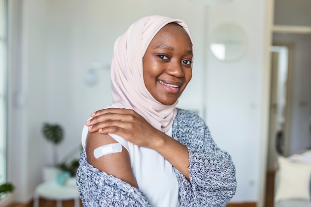 Pansement adhésif sur le bras après injection de vaccin ou de médicament, PLÂTRE DE BANDAGES ADHÉSIFS - Équipement médical, Bandage adhésif à mise au point douce sur un brachium de femme africaine musulmane après la vaccination contre le covid-19