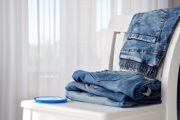 Pantalon jeans élégant bleu plié sur une chaise blanche avec fenêtre en tulle