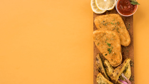 Panure de filet de poulet et de quartiers de pommes de terre sur une planche de bois