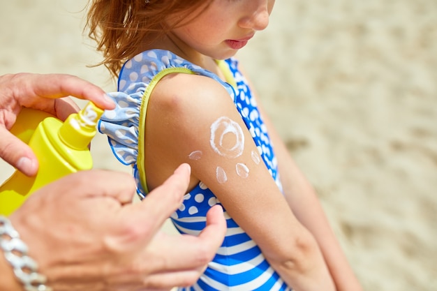 Papa appliquant un écran solaire à sa fille sur la plage. Vacances d'été.