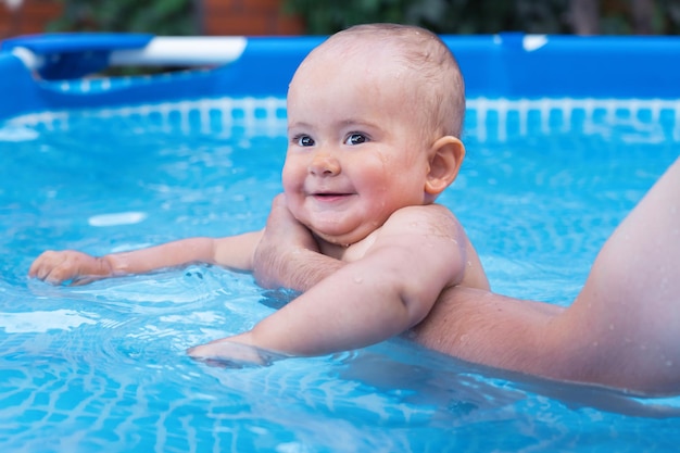 Papa apprend à un bébé à nager dans une piscine à ossature en le soutenant avec sa main