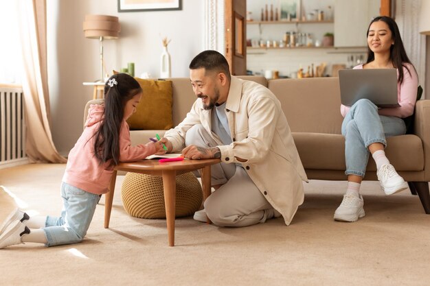 Papa asiatique et sa petite fille dessinent pendant que maman travaille à l'intérieur