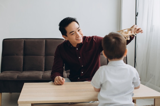 Papa asiatique et son mignon petit fils jouant avec un avion en bois dans une pièce lumineuse