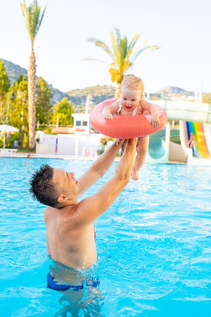 Papa et bébé dans un cercle gonflable dans la piscine avec toboggans en été s'amusent à nager en se relaxant et en s'amusant à jeter l'enfant