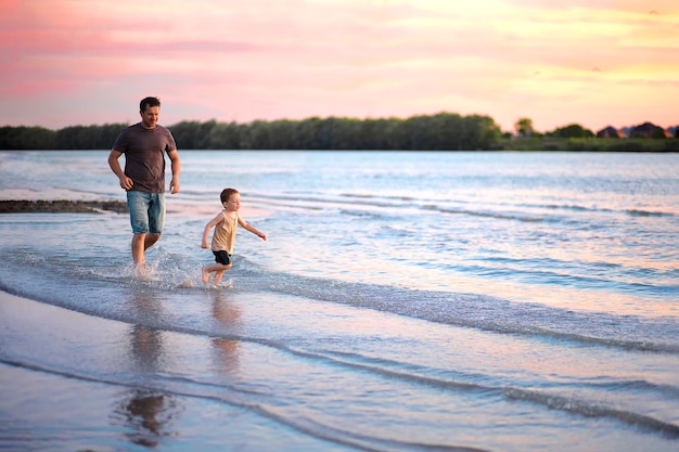 Papa court après son fils le long de la rive au coucher du soleil