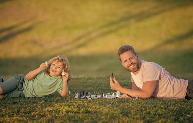 Papa et enfant jouent au jeu de logique père et fils jouant aux échecs sur l'herbe dans le parc fête des pères