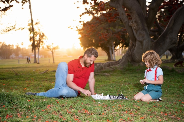 Papa et enfant jouent à un jeu de logique. père et fils jouant aux échecs sur l'herbe dans le parc. fête des pères. famille heureuse. parentalité et enfance. échec et mat. passer du temps ensemble. stratégique et tactique.