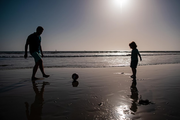 Papa et enfant s'amusant à l'extérieur père et fils jouent au football ou au football sur la plage en été fami