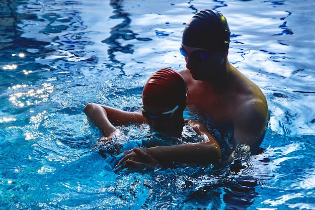 Papa et entraîneur apprennent à son fils à nager en s'amusant à jouer et à éclabousser dans une piscine bleue