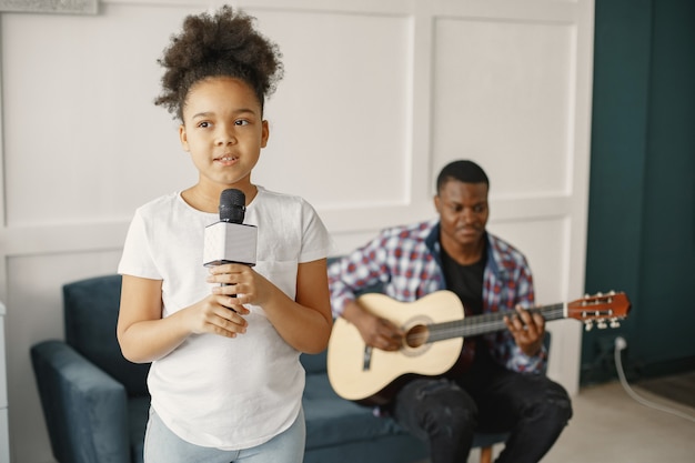 Papa est assis avec une guitare et sa fille avec un microphone