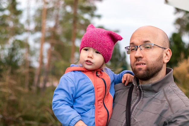 Papa étreignant tenant sa petite fille dans les bras sur fond flou d'arbres dans le parc