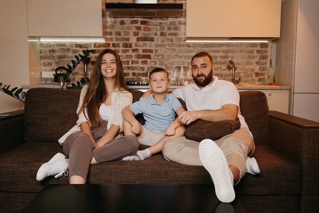 Papa, fils et maman regardent avec intérêt la télévision sur le canapé de l'appartement