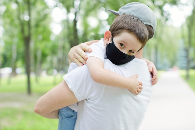 Papa et fils portant des masques noirs marchant dans le parc Concept de distanciation sociale et de quarantaine