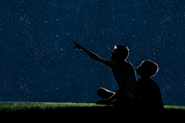 Papa et fils s'assoient sur l'herbe la nuit et regardent le ciel nocturne