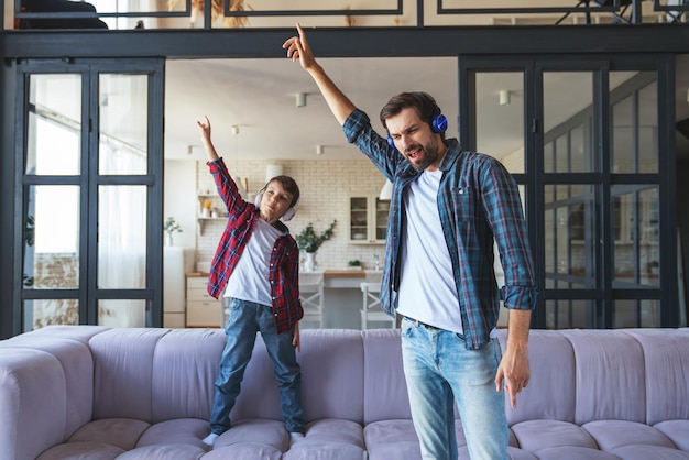 Papa heureux et son petit fils écoutent de la musique sur des écouteurs et dansent à la maison dans le salon