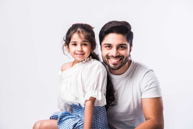 Papa indien aimant embrassant la petite fille adorable mignonne assise sur les genoux ou sur le dos - concept montrant l'amour, les soins, la personne la plus proche, la fête des pères