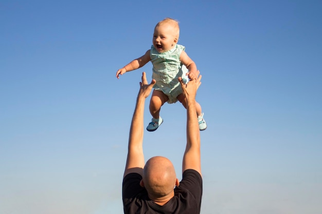 Papa jette son enfant contre le ciel bleu. Jeu de concept avec des enfants, famille heureuse.