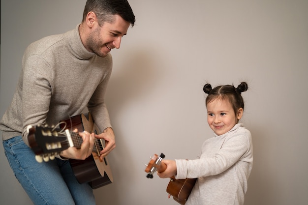 Papa joue de la guitare avec sa fille. L'enfant apprend à jouer d'un instrument de musique avec un tuteur. Duo musical d'un père avec un enfant.