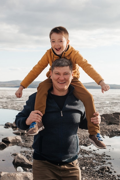 Papa joue avec son fils au bord de la rivière. Un beau père et son fils s'amusent à jouer et à sourire par une journée ensoleillée. L'enfant est dans les bras de son père. Loisirs de plein air.