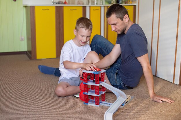 Un papa joyeux joue avec un garçon mignon à la maison dans des voitures