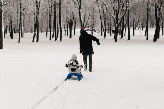 Papa monte un garçon mignon dans un traîneau dans la famille d'hiver de style de vie actif de neige