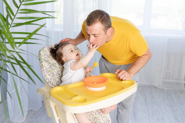 Papa nourrit sa petite fille dans une chaise haute concept d'aliments pour bébés paternité heureuse