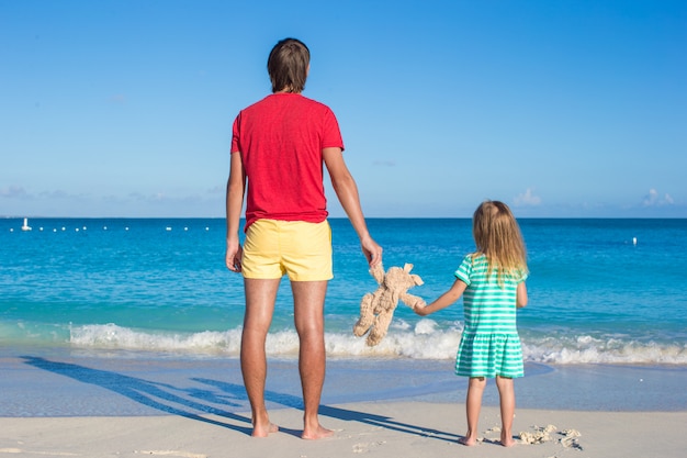 Papa avec petit bébé tenant une peluche sur une plage exotique