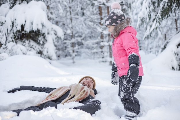 Papa et petite fille allongée sur la neige dans le parc d'hiver