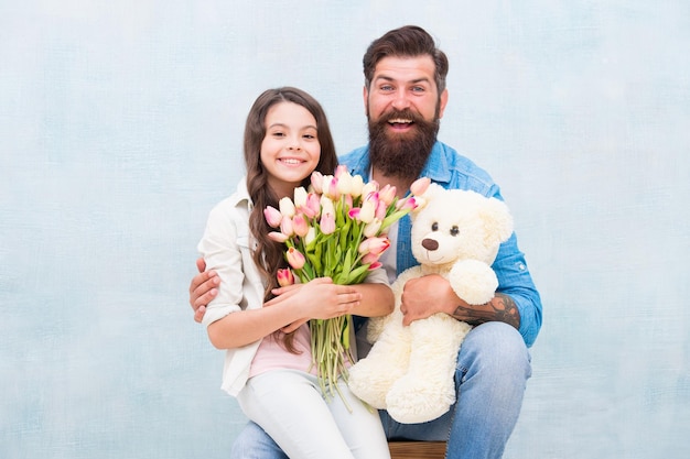 Papa et petite fille s'embrassent avec bouquet de fleurs de tulipe printanière et ours en peluche jouet journée des enfants