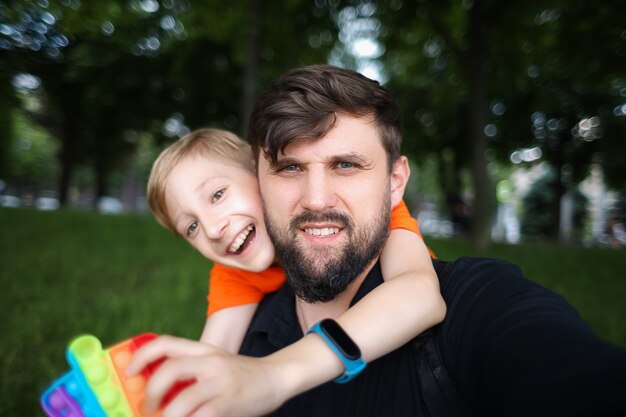 Papa regarde la caméra et prend un selfie, l'enfant le serre dans ses bras par le cou et rit joyeusement