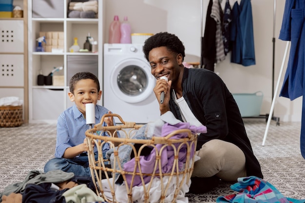 Papa s'amusant avec son fils tout en nettoyant les tâches ménagères homme chantant au rouleau de nettoyage