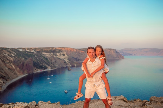 Papa et sa fille au bord de la falaise profiter de la vue sur le rocher du sommet de la montagne au coucher du soleil