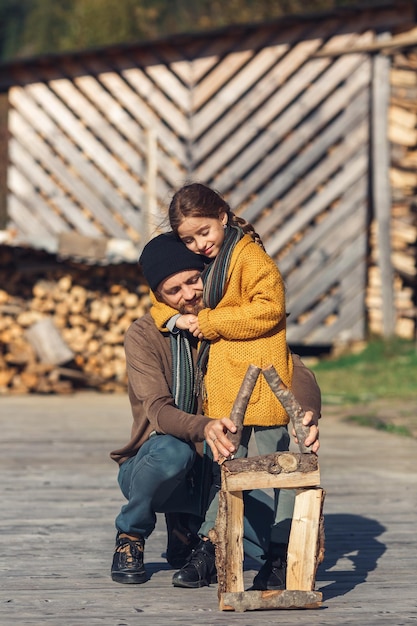 Papa Et Sa Fille Construisent Ensemble Une Maison En Rondins De Jouets Sur Une Terrasse Dans Les Montagnes Par Une Journée D'automne Ensoleillée