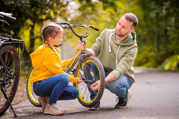 Papa et sa fille inspectent la roue du vélo adolescent des enfants sur le chemin d'automne du parc